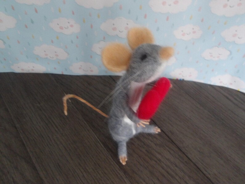 Puede incluir: Un rat&oacute;n de fieltro gris que sostiene un coraz&oacute;n de fieltro rojo. El rat&oacute;n tiene una cola larga y delgada y un par de orejas grandes y redondas.