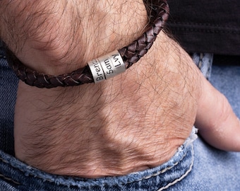 Op de afbeelding: Een bruin leren armband met zilveren kralen gegraveerd met de namen "Brenna", "Sam" en "Lily".
