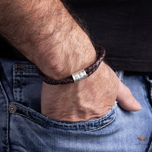 K&ouml;nnte beinhalten: Ein braunes Lederarmband mit einer silbernen Perle, die mit den Namen "Bren", "Sam" und "Liv" graviert ist.