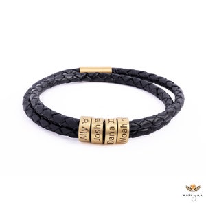 K&ouml;nnte beinhalten: Schwarzes Lederarmband mit geflochtenem Design und vier goldenen Perlen, die mit den Namen Ally, Josh, Dana und Noah graviert sind.