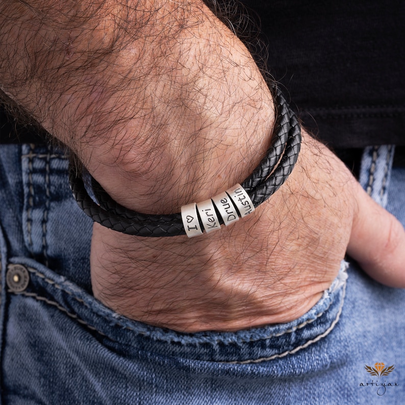K&ouml;nnte beinhalten: Ein schwarzes Lederarmband mit silbernen Perlen, auf denen "I love", "Keri", "Drue" und "Austin" steht.