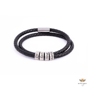 K&ouml;nnte beinhalten: Schwarzes Lederarmband mit einem silbernen Verschluss und vier silbernen Perlen, auf denen die Namen "I love", "Keri", "Drue" und "Austin" eingraviert sind.