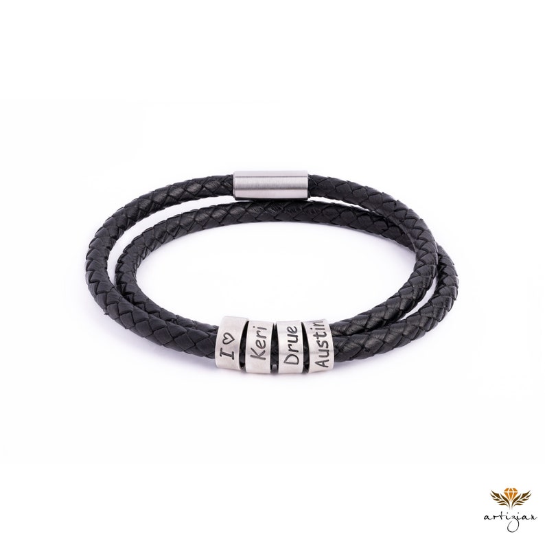K&ouml;nnte beinhalten: Schwarzes Lederarmband mit einem silbernen Verschluss und vier silbernen Perlen, auf denen die Namen "I love", "Keri", "Drue" und "Austin" eingraviert sind.