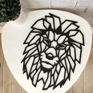 May include: A black wall art piece shaped like a lion head, featuring a geometric design with sharp, angular lines that form the mane and facial features. The object is flat and constructed with a cutout style, displaying a solid black color throughout.