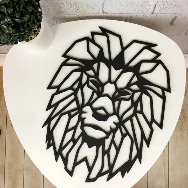 May include: A black wall art piece shaped like a lion head, featuring a geometric design with sharp, angular lines that form the mane and facial features. The object is flat and constructed with a cutout style, displaying a solid black color throughout.