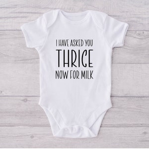 May include: White baby bodysuit featuring the black text "I HAVE ASKED YOU THRICE NOW FOR MILK". The onesie has short sleeves and a simple design, suitable for a newborn.