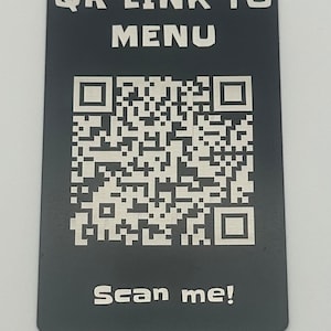 Puede incluir: Un letrero de metal negro con un código QR y el texto "QR LINK TO MENU" y "Scan me!" en blanco.