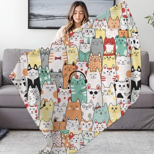 May include: A colorful throw blanket featuring a repeating pattern of cartoon cats in various colors and designs. The cats have different expressions and accessories, such as bow ties and sunglasses. The blanket is draped over a gray sofa.