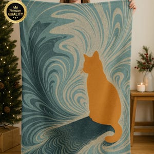 May include: A teal and beige throw blanket featuring an orange cat silhouette. The blanket has a swirling pattern design. The words "Premium Quality" are in a gold seal in the upper left corner. The blanket is held up by a person.
