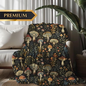 Op de afbeelding: Een zwarte deken met een herhalend patroon van paddenstoelen in rood, bruin en beige, met groene en oranje bladeren. Het woord "PREMIUM" staat in gouden letters op een zwarte banner.