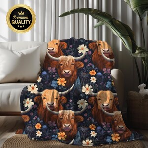 May include: A cozy throw blanket featuring a repeating pattern of Highland cows with long, shaggy brown fur, set against a dark blue background with floral accents. The blanket is draped over a white sofa, creating a warm and inviting aesthetic.