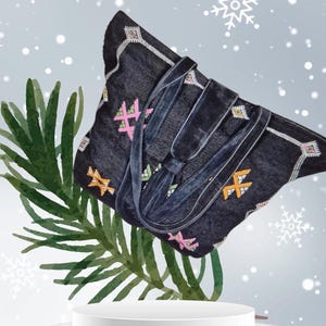 Könnte beinhalten: Eine schwarze Tragetasche mit bunten, gestickten geometrischen Mustern. Die Tasche hat einen langen Riemen und steht auf einer weißen Plattform.