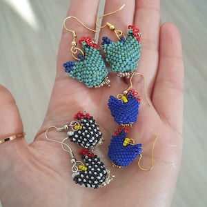 Peut inclure: Un ensemble de cinq boucles d'oreilles en forme de poulets en perles. Les boucles d'oreilles sont faites de perles colorées et ont des crochets dorés. Les poulets sont de différentes couleurs, notamment bleu, noir, blanc et rouge.