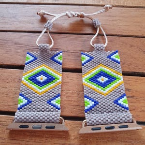May include: A grey, blue, green, white and yellow beaded Apple Watch band with a geometric pattern. The band is adjustable with a string tie.