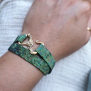 May include: A double-strand bracelet with a green iridescent finish and a gold-toned clasp. The clasp features a decorative floral design.
