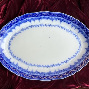 Puede incluir: Plato ovalado para servir con centro blanco y borde floral azul. El borde presenta un diseño detallado en azul y dorado. El plato mide aproximadamente 40 cm de largo y 30 cm de ancho, ideal para servir comida en una cena.