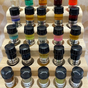 May include: A wooden display stand holding numerous small glass fragrance bottles with black caps. The bottles contain various colored liquids and labels with fragrance names like "Black Love" and "Baby Pow".