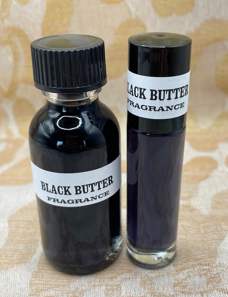 May include: Two bottles of Black Butter fragrance oil. One bottle is a clear glass roll-on bottle with a black cap. The other bottle is a clear glass bottle with a black cap and a black label that says "Black Butter Fragrance".