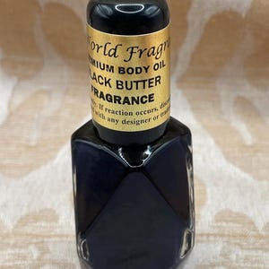 May include: A small, dark blue glass bottle with a gold label that reads "World Fragrance Premium Body Oil Black Butter Fragrance".