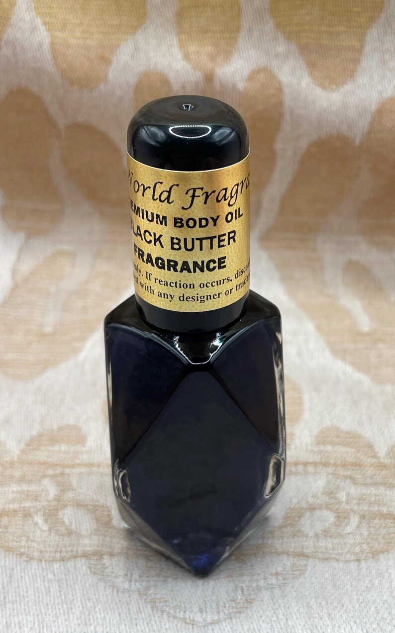 May include: A small, dark blue glass bottle with a gold label that reads "World Fragrance Premium Body Oil Black Butter Fragrance".