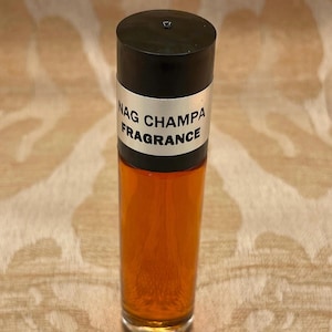 Pu&ograve; includere: Una bottiglia di vetro trasparente con un tappo nero e un'etichetta argentata che recita "Nag Champa Fragrance". La bottiglia &egrave; piena di un liquido ambrato scuro.