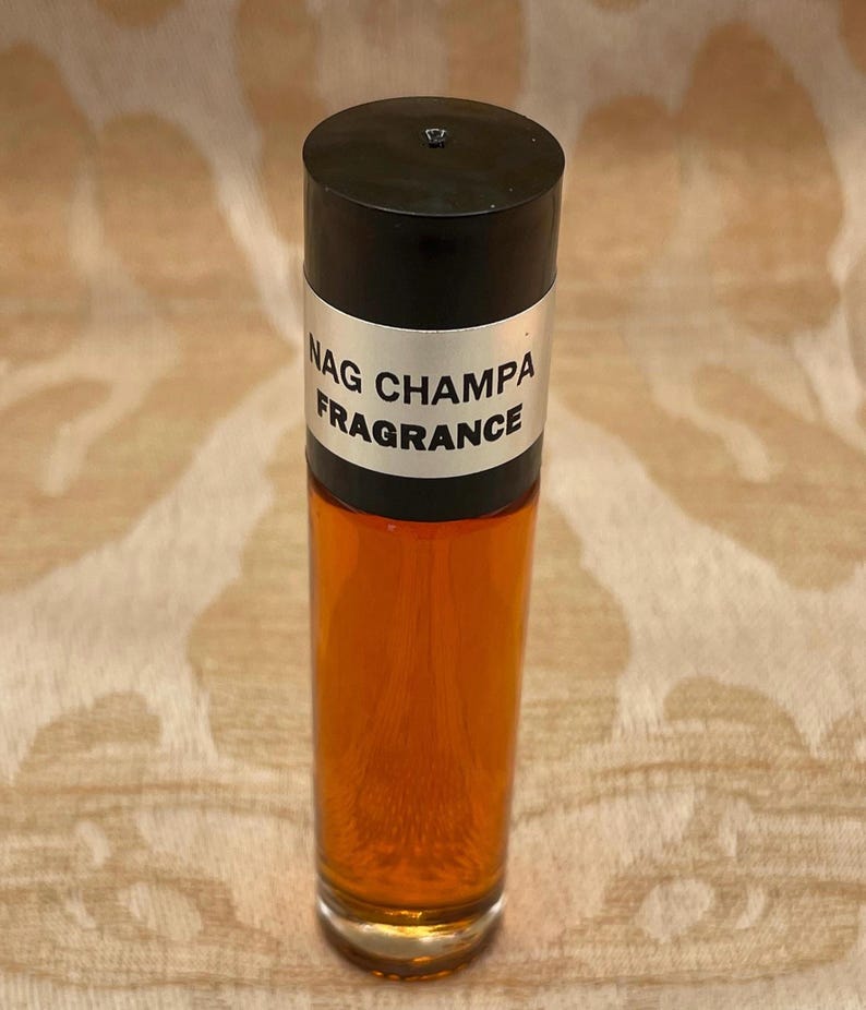 Pu&ograve; includere: Una bottiglia di vetro trasparente con un tappo nero e un'etichetta argentata che recita "Nag Champa Fragrance". La bottiglia &egrave; piena di un liquido ambrato scuro.