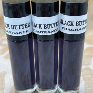 May include: Three glass bottles with black caps and white labels that read "Black Butter Fragrance". The bottles are filled with a dark purple liquid.