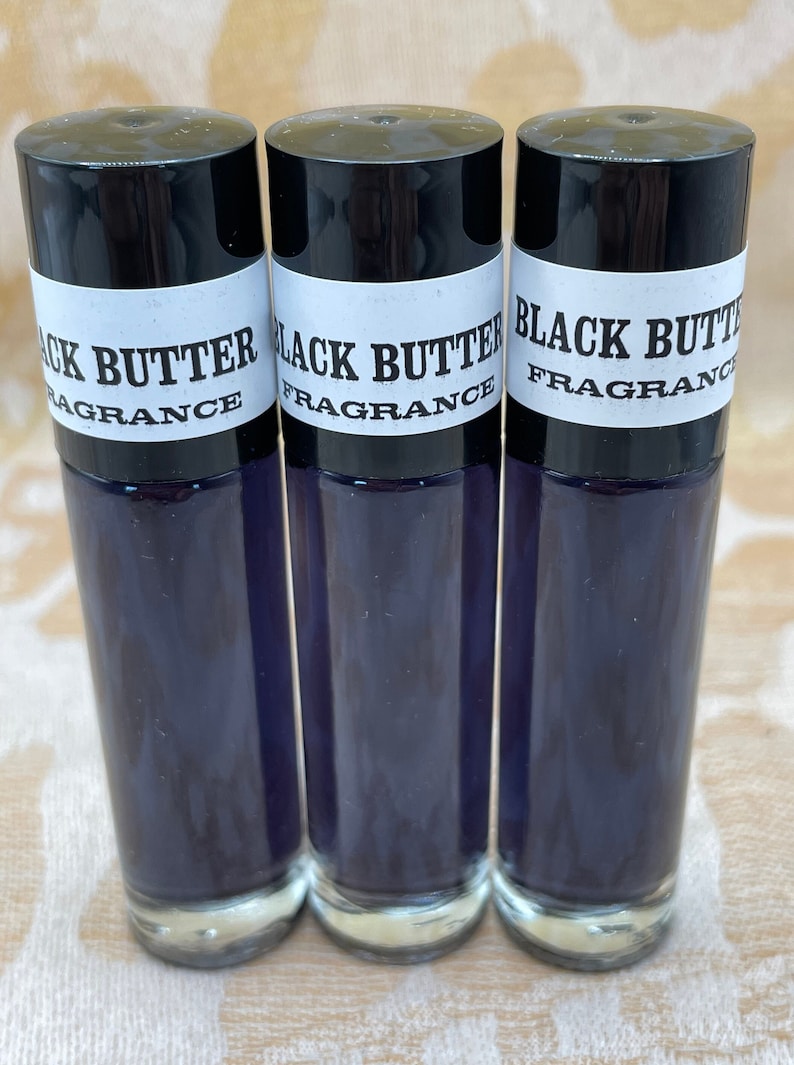 May include: Three glass bottles with black caps and white labels that read "Black Butter Fragrance". The bottles are filled with a dark purple liquid.