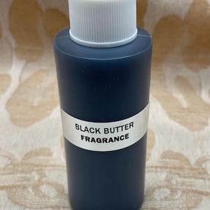 May include: A small, dark blue glass bottle with a white cap. The bottle has a white label that reads "BLACK BUTTER FRAGRANCE".