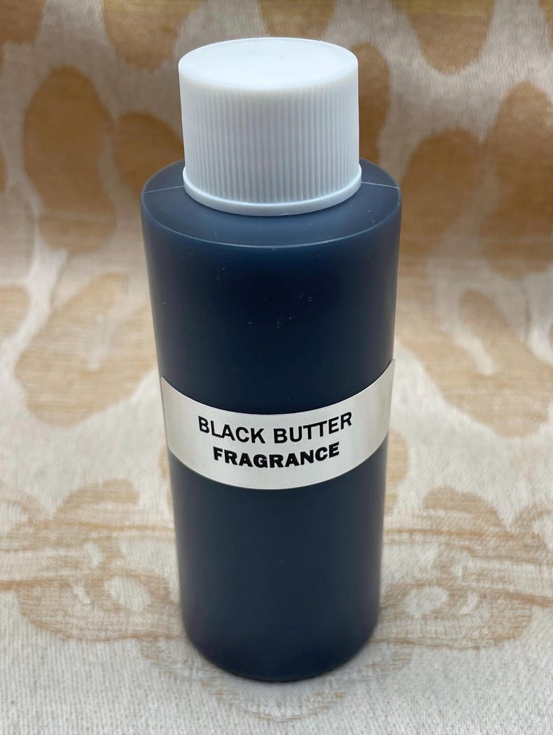 May include: A small, dark blue glass bottle with a white cap. The bottle has a white label that reads "BLACK BUTTER FRAGRANCE".
