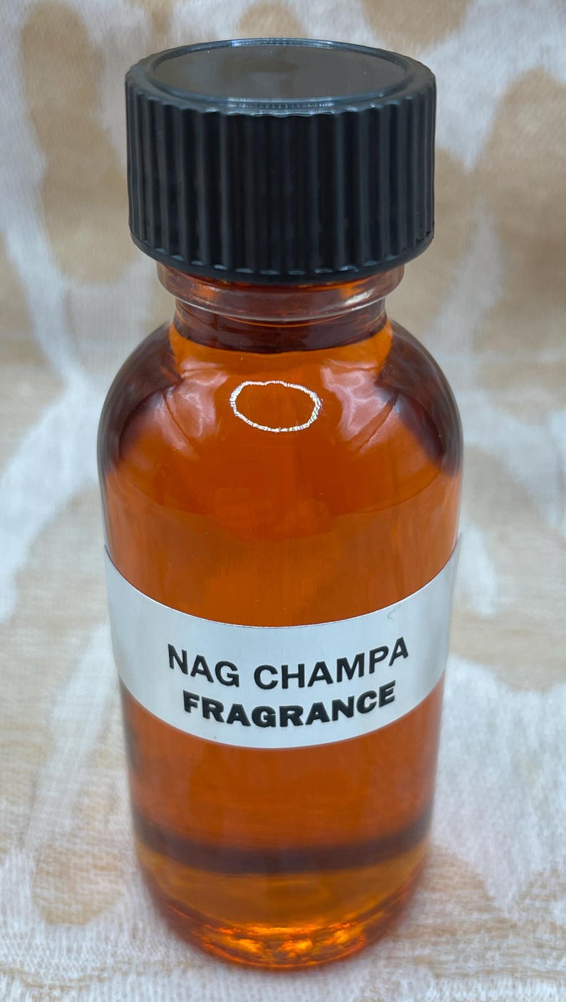 Pu&ograve; includere: Una bottiglia di vetro trasparente con un tappo a vite nero riempita di un liquido marrone. La bottiglia ha un'etichetta bianca con il testo "NAG CHAMPA FRAGRANCE".
