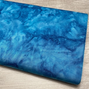 May include: A folded piece of fabric with a blue tie-dye pattern. The fabric has shades of light and dark blue, creating a watercolor effect. The fabric is likely cotton or a similar material.