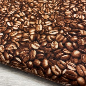 May include: Close-up of a fabric with a repeating pattern of coffee beans. The beans are various shades of brown, creating a textured and detailed design. The fabric appears to be a cotton or similar material, suitable for various craft projects.
