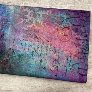May include: A piece of fabric with a distressed, vintage design. The fabric features a blend of colors, including purple, teal, and pink, with a faded script and floral pattern. The word "THE" is visible in the upper right corner.