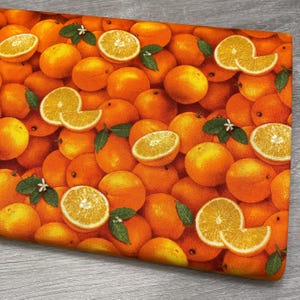May include: A fabric with a vibrant orange pattern featuring whole oranges and orange slices. Green leaves and white blossoms are interspersed among the fruit. The design creates a fresh, summery feel, perfect for kitchen or home decor projects.