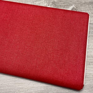 May include: A folded stack of red fabric with a textured surface. The fabric has a solid color and appears to be a medium weight material. The edges of the fabric are white.