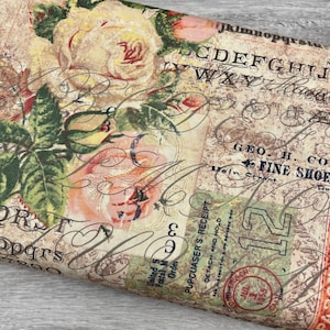 May include: Vintage-style fabric with a floral design of pink and cream roses, green leaves, and script. The fabric has a distressed appearance with text elements, including "FINE SHOE" and "PUPCUASERS RECEIPT".