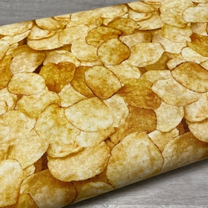 May include: Fabric with a repeating pattern of golden-brown potato chips. The chips vary in size and shape, with some showing darker, toasted edges. The fabric has a slightly textured appearance, suggesting a cotton or linen blend.