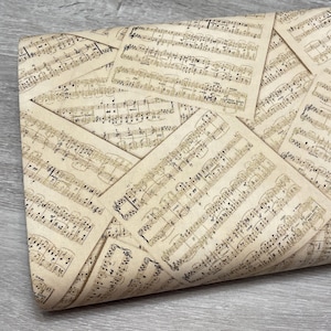 May include: A roll of decorative paper featuring a vintage sheet music design. The paper has a beige background with printed musical notes and symbols in black ink. The paper is folded over, revealing the pattern.