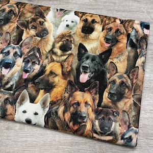 May include: A rectangular fabric featuring a collage of German Shepherd dog faces. The dogs display a variety of colors, including black, brown, tan, and white. Some dogs have their tongues out. The overall theme is dogs.