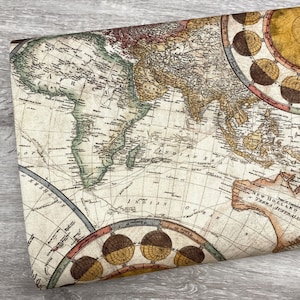 May include: A folded piece of fabric featuring a vintage world map design. The map is in shades of beige, brown, and green, with intricate details and cartographic elements. Decorative circular elements with brown and yellow accents are visible.