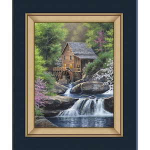 May include: A framed painting depicts a serene landscape with a wooden water mill nestled among lush greenery and cascading waterfalls. The mill's windows glow with warm light, and the scene is framed by a gold border and a dark blue mat.