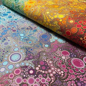 May include: Close-up of two fabric pieces with a colorful, abstract pattern. The top fabric displays a gradient of colors from green to red, while the bottom fabric features a mix of blue, purple, and pink circles on a neutral background. The design is reminiscent of bubbles.