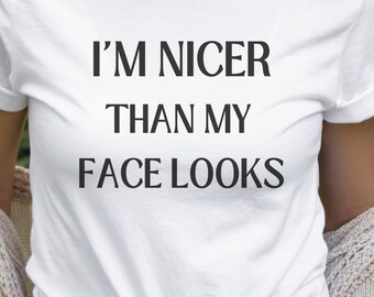 May include: White t-shirt with the text "I'm nicer than my face looks" printed in black.