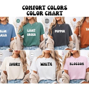 Op de afbeelding: Een kleurenkaart toont zes t-shirts in verschillende kleuren: blue jean, lichtgroen, peper, yam, ivoor, wit en blossom. Elk shirt heeft de kleurnaam in een retro lettertype gedrukt. De tekst "COMFORT COLORS COLOR CHART" staat bovenaan.