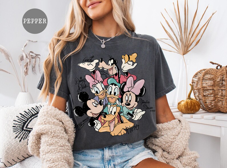 May include: Dark gray t-shirt featuring a graphic of Disney characters including Mickey Mouse, Minnie Mouse, Donald Duck, Daisy Duck, Goofy, and Pluto. The shirt has the text "Daisy Duck", "Minnie Mouse", and "Goofy".