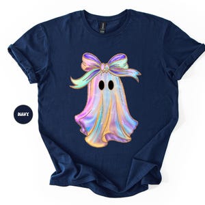Op de afbeelding: Marineblauw t-shirt met een kleurrijk spookontwerp en een strik. De geest heeft een glinsterende, iriserende uitstraling met zwarte ogen. Het woord "NAVY" is gedrukt op een marineblauwe cirkel.