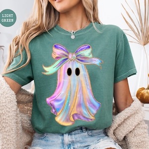 Op de afbeelding: Lichtgroen T-shirt met een kleurrijk spookontwerp en een grote strik. Het spook is afgebeeld in tinten paars, blauw en geel met zwarte ogen. De strik is een mix van paars, groen en geel. Het shirt heeft een comfortabele pasvorm.