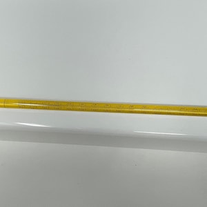 Puede incluir: Un termómetro de vidrio amarillo con una punta azul y un extremo de metal plateado. El termómetro está marcado con números y líneas.
