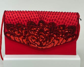 Könnte beinhalten: Eine rote Abendtasche mit Pailletten, einem Klappverschluss und einem kurzen Kettenriemen.